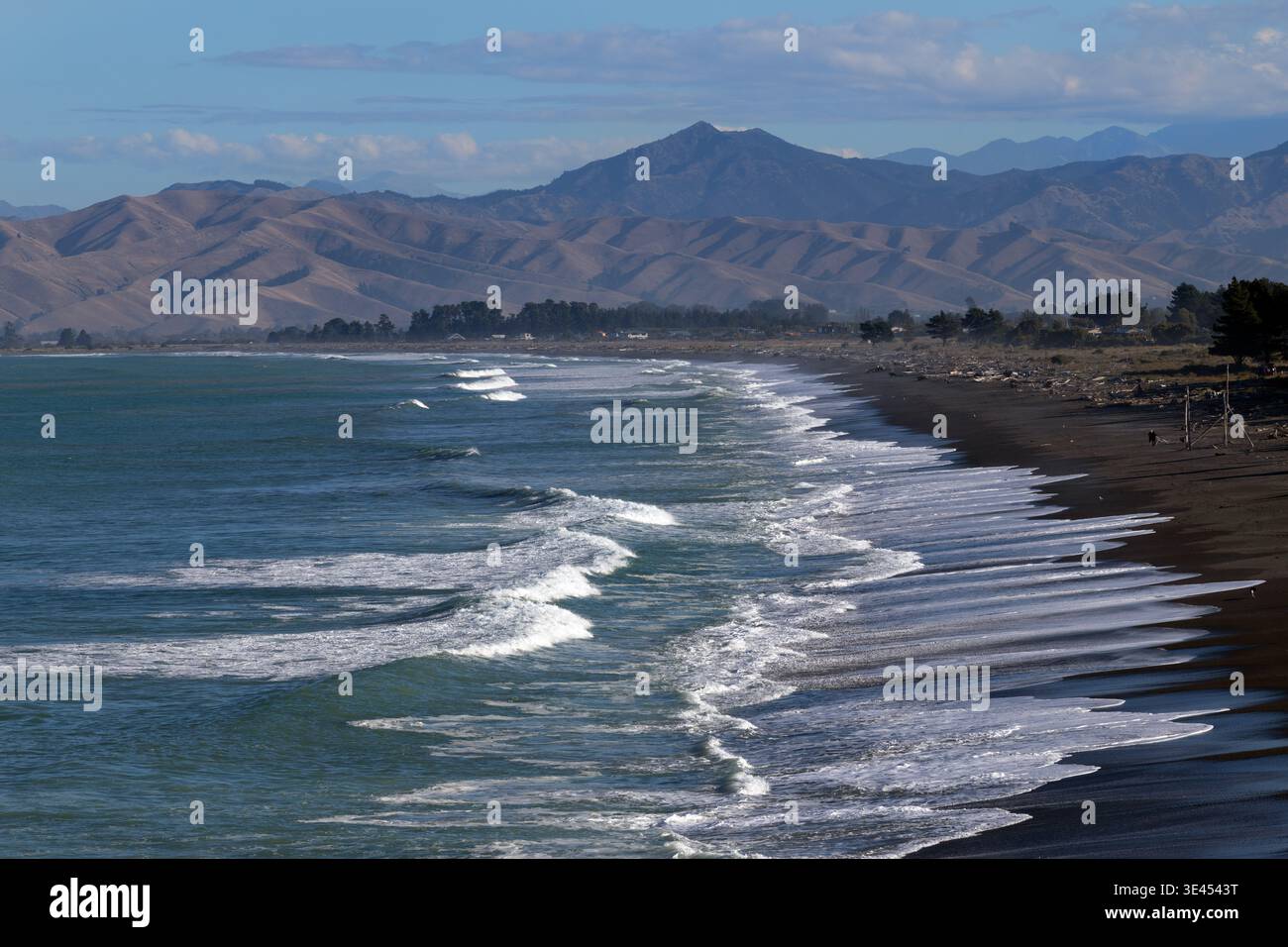 Onde che si infrangono lungo una spiaggia di sabbia scura a Rarangi con colline costiere oltre, Marlborough, South Island, nuova Zelanda Foto Stock