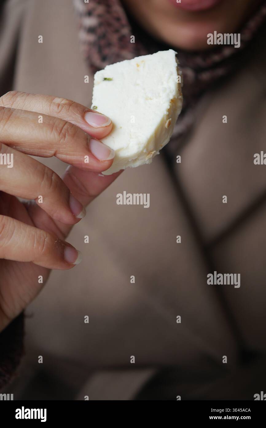 La persona ama un pezzo di formaggio mentre indossa una sciarpa calda Foto Stock