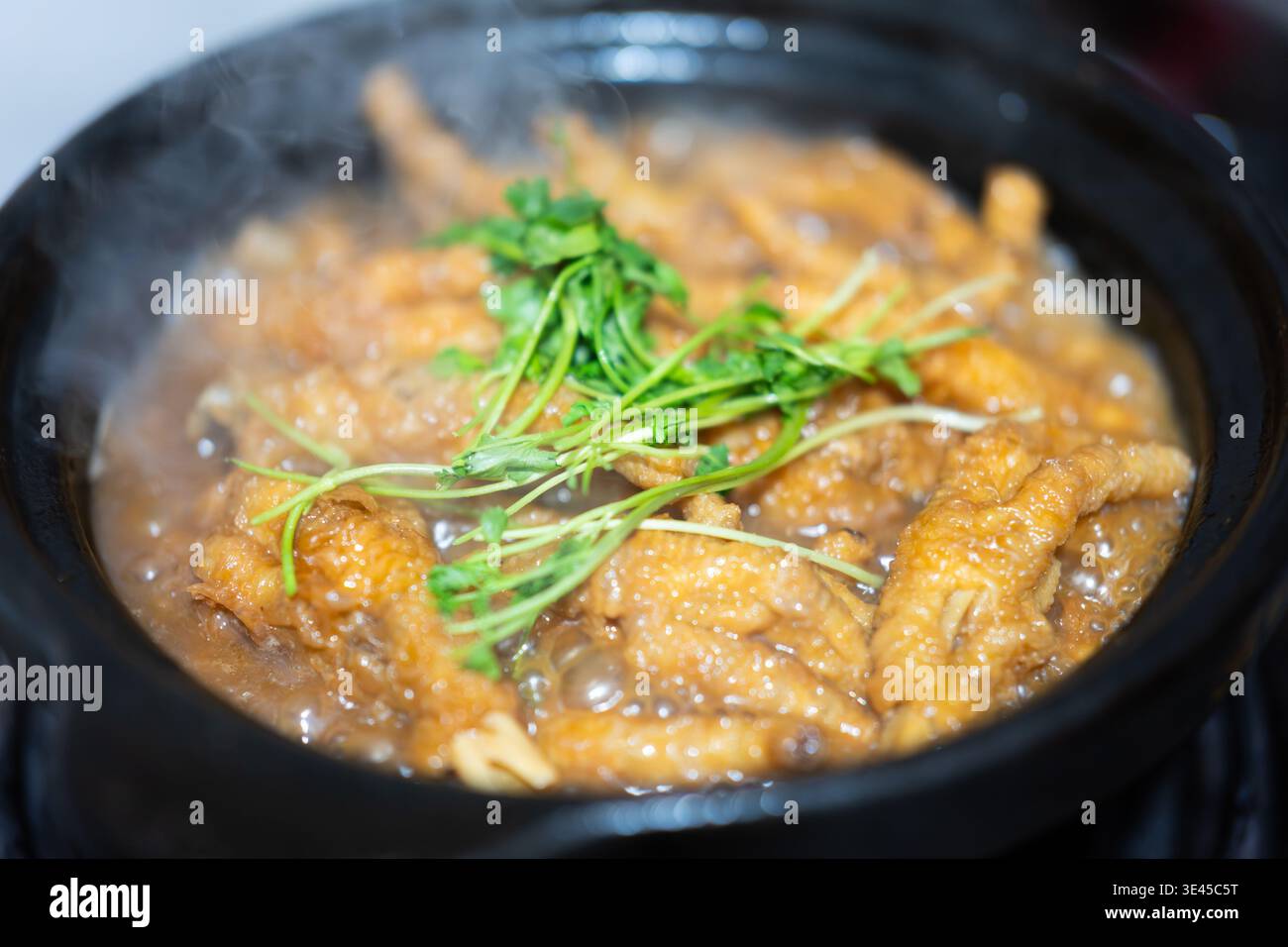 Piedini di pollo in stile cantonese fumante in pentola di argilla, guarniti con coriandolo fresco, serviti a Hong Foto Stock