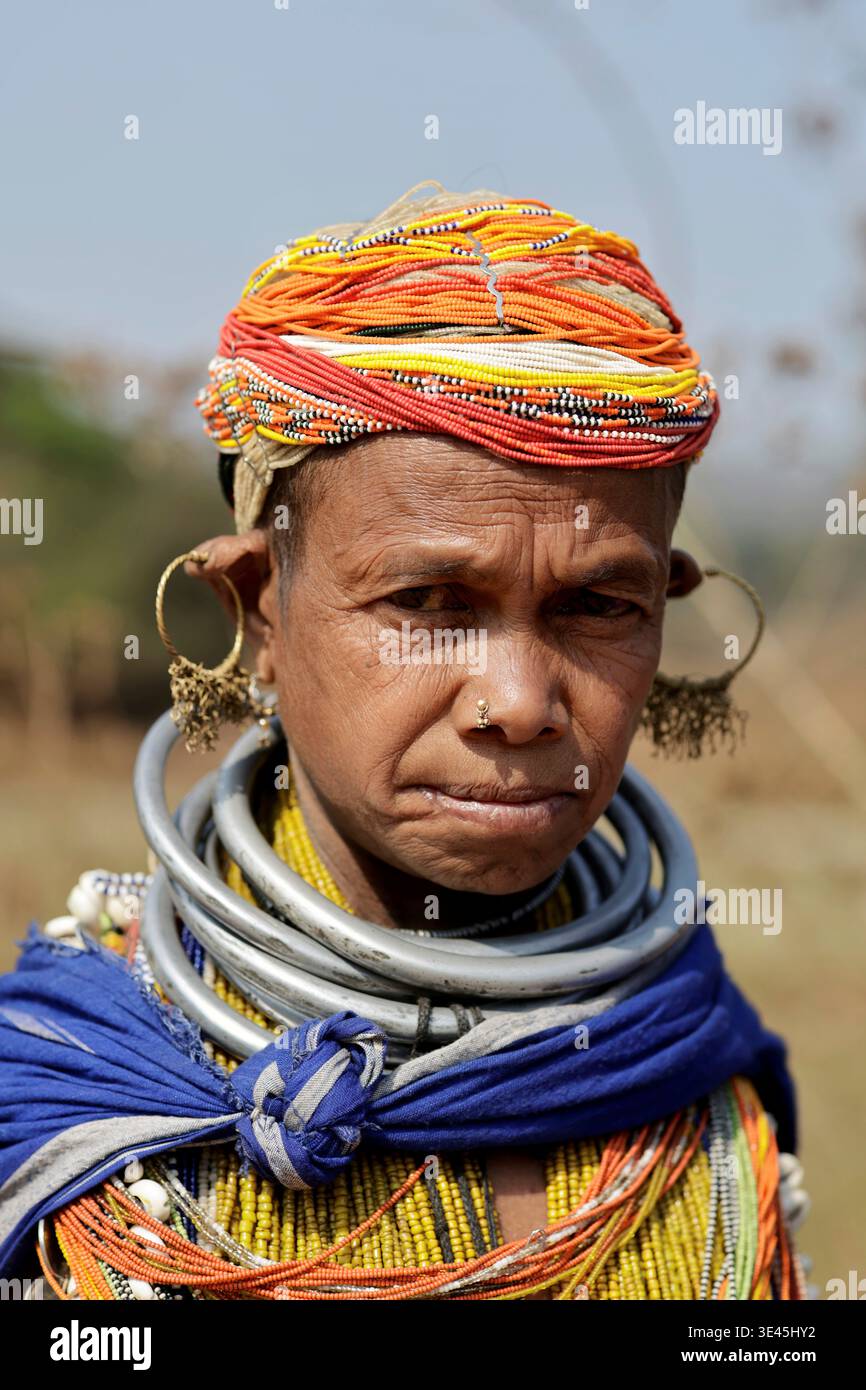 Odisha, India - 26 marzo 2026: Vista di una donna adornata da vivaci copricapi arancioni, bianchi e blu, in contrasto con pesanti collane in argento e grandi Foto Stock