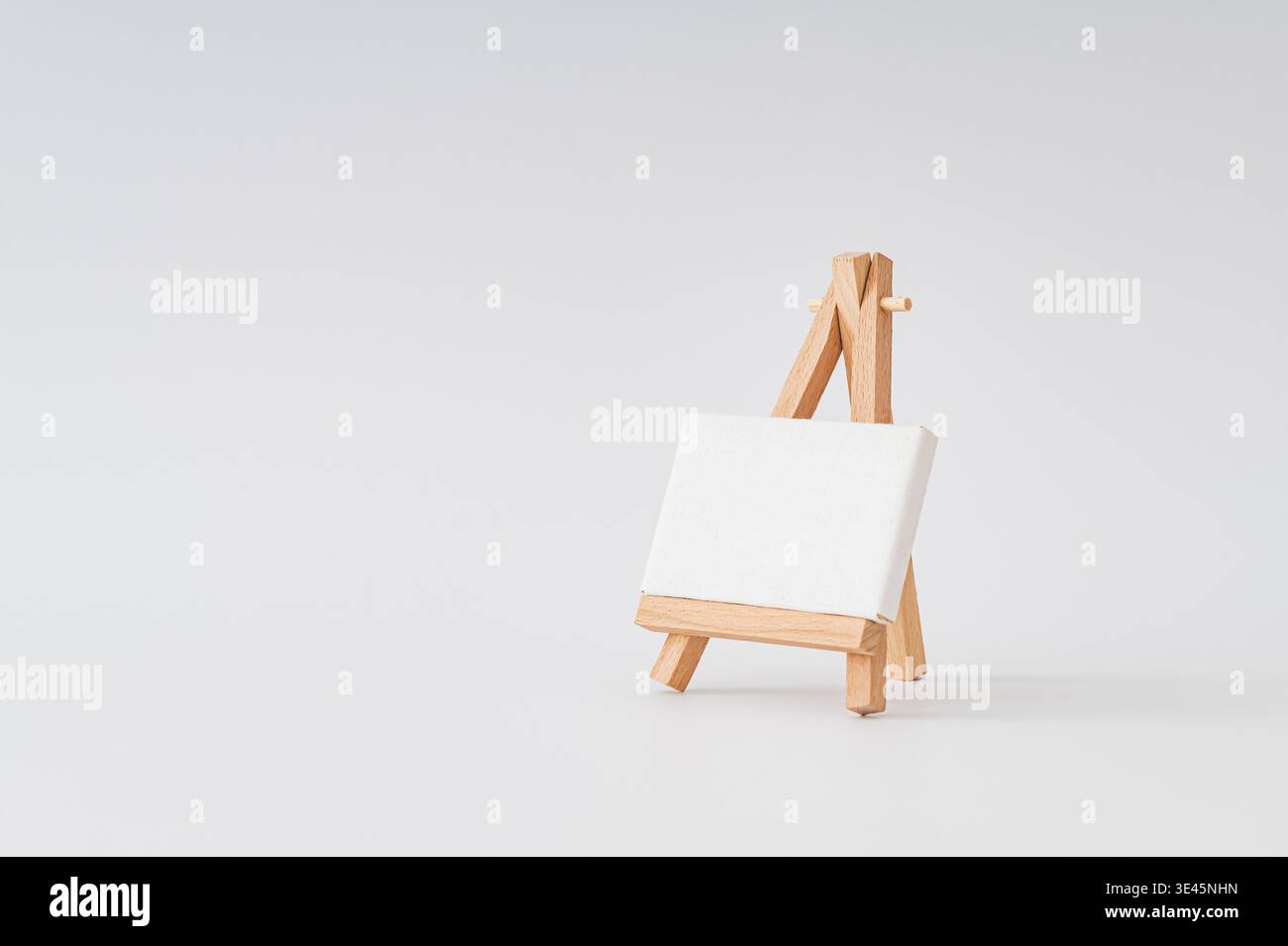 Tela vuota su cavalletto in legno su sfondo bianco. Mockup artistico minimalista. Idea di presentazione del branding. Spazio di copia creativo. Foto Stock
