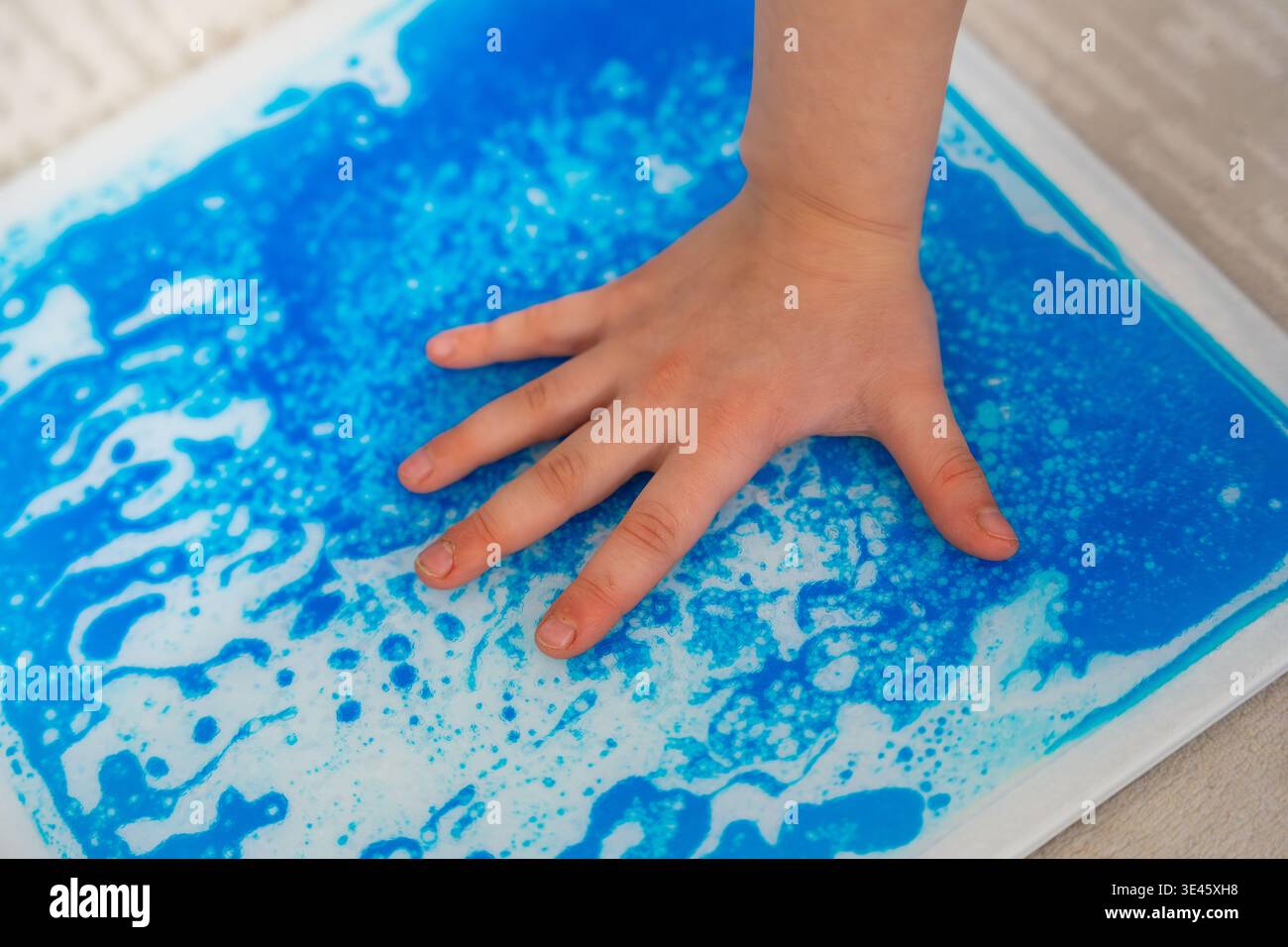 Tappetino colorato in gel sensoriale per bambini che preme la mano per creare motivi in movimento durante il gioco tattile. Stimolazione sensoriale e concetto di terapia occupazionale per Foto Stock