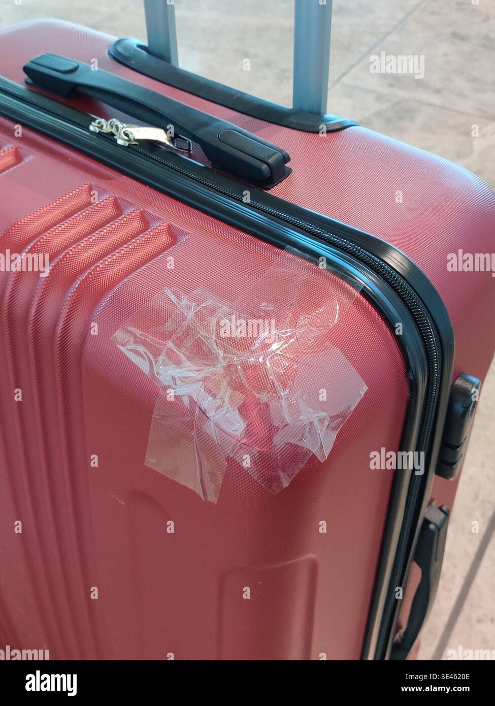 Una valigia da viaggio rigida rossa con segni di usura e danni visibili riparata con nastro adesivo trasparente. Foto Stock