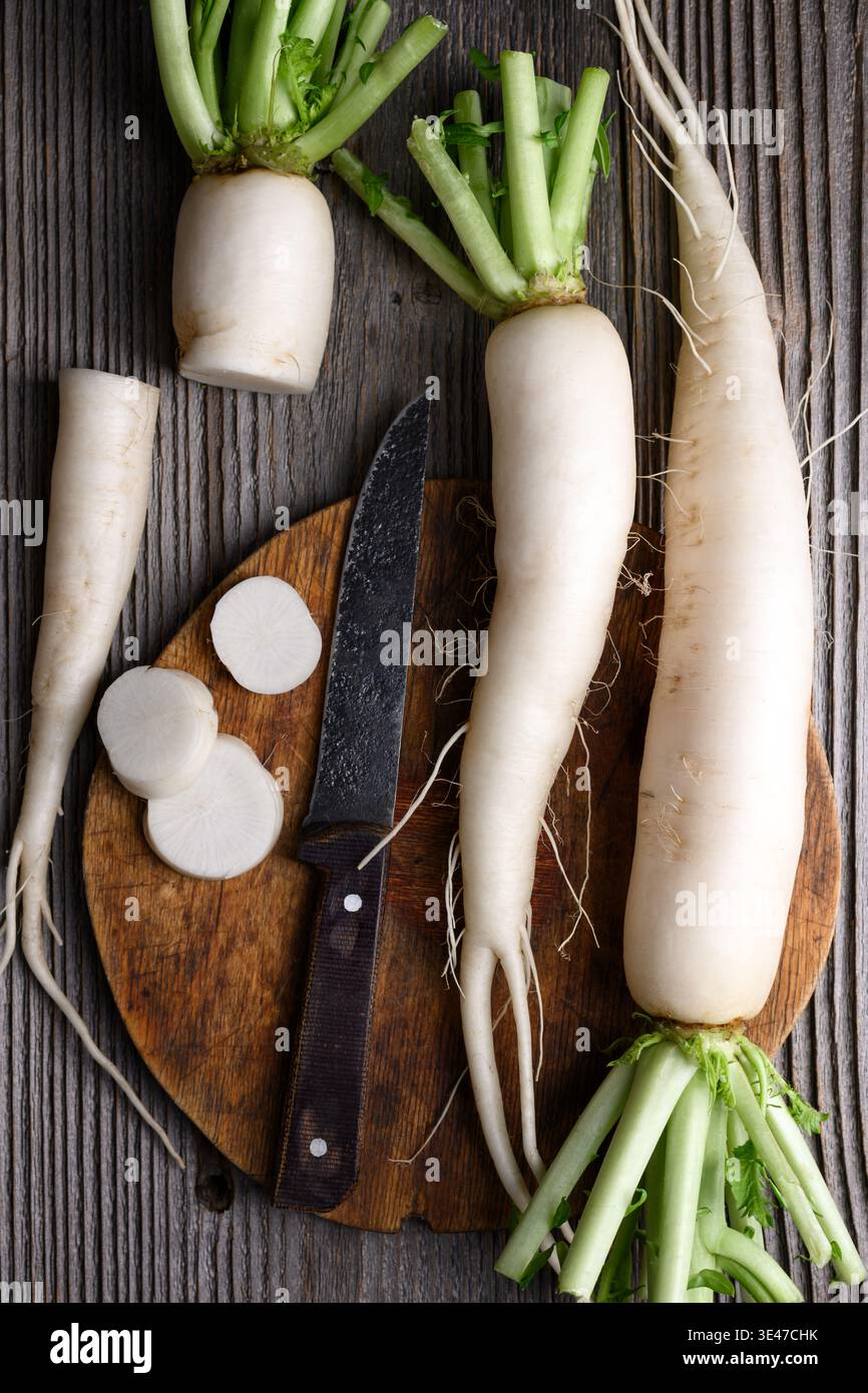 Ravanello daikon a fette con coltello su tavola rustica, ravanello bianco, ingredienti da cucina Foto Stock