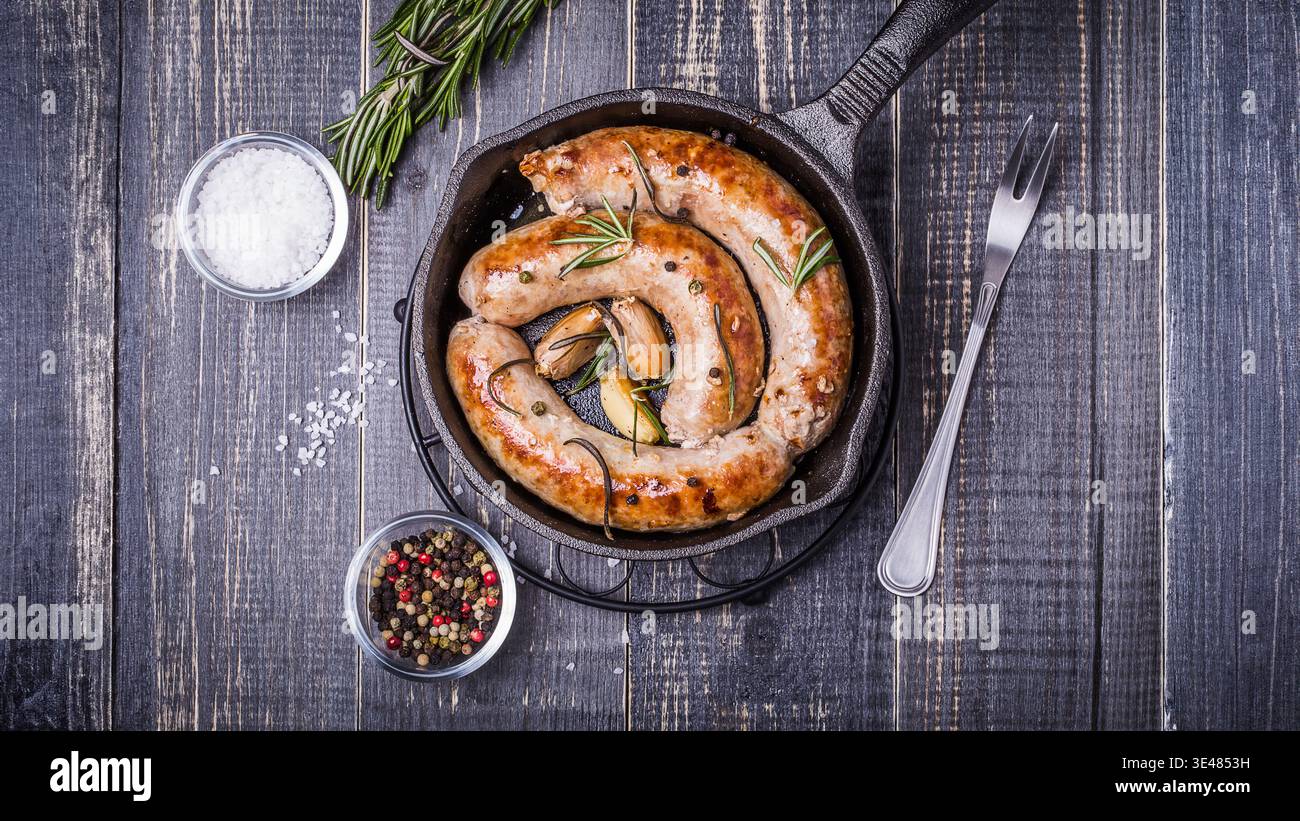 Salsicce fritte in stile Сountry con rosmarino, aglio su fondo scuro in legno Foto Stock