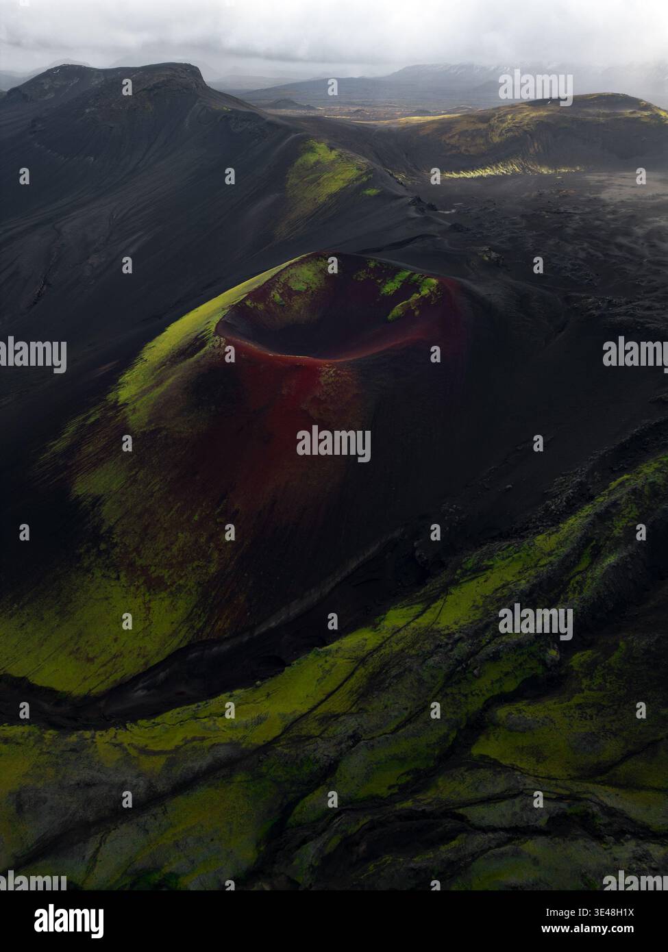 Vista aerea di un cratere vulcanico con suolo rosso e muschio verde circondato da un paesaggio vulcanico nero in Islanda. Foto Stock