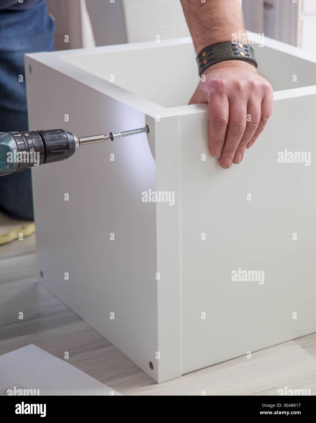 Uomo che assembla l'armadio bianco con trapano a batteria, avvitando la vite nel pannello dei mobili, fai da te per il miglioramento della casa, assemblaggio di mobili in confezioni piatte, tuttofare Foto Stock