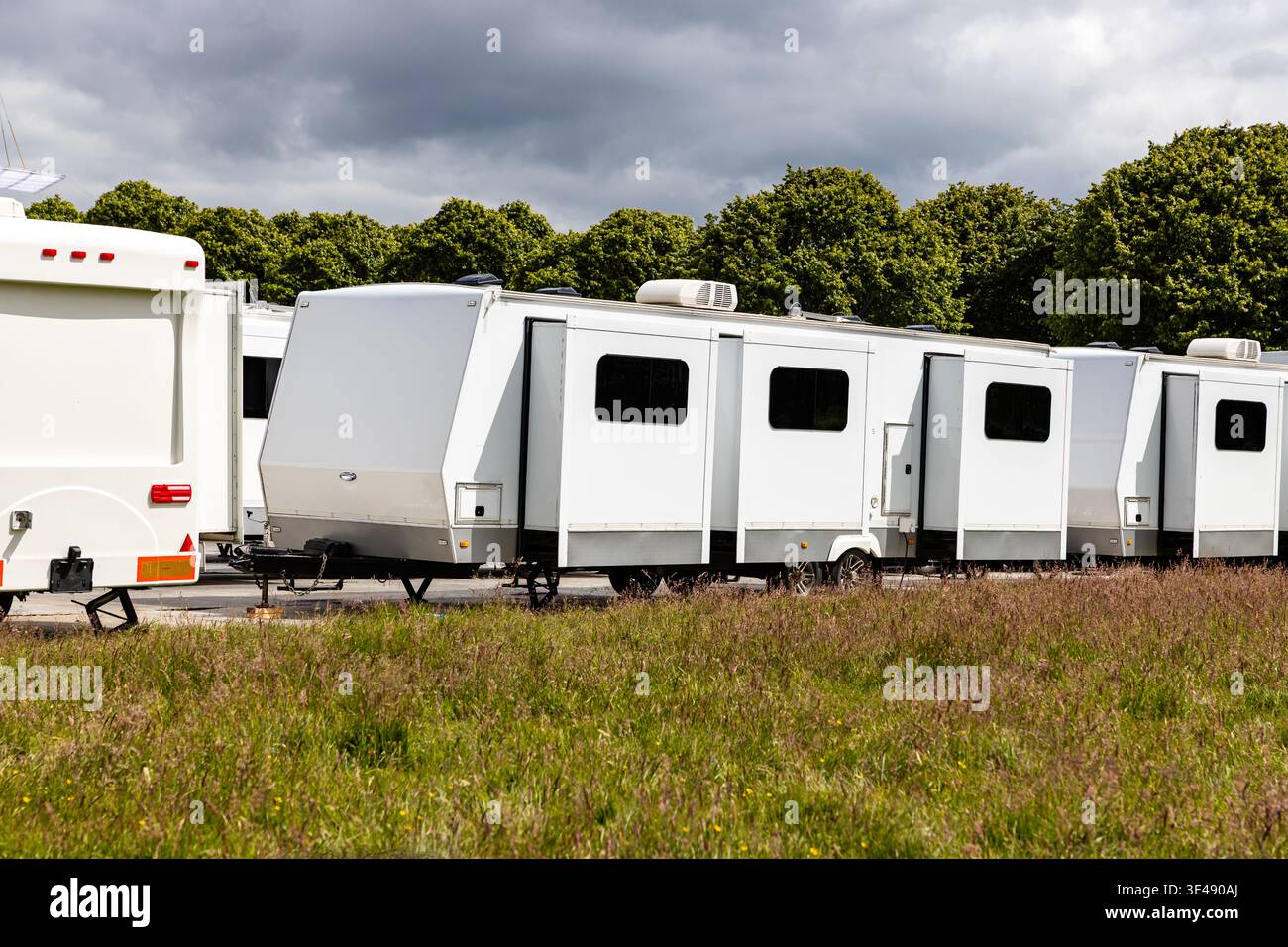 Servizi e servizi di localizzazione per TV e film, una fila di unità espandibili bianche o rimorchi da viaggio parcheggiati su un terreno solido e temporaneo con alberi Foto Stock
