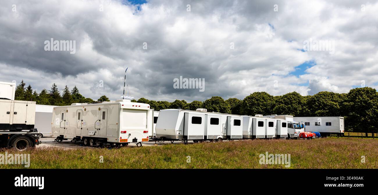 Servizi e servizi di localizzazione per TV e film, una fila di unità espandibili bianche o rimorchi da viaggio parcheggiati su un terreno solido e temporaneo con alberi Foto Stock
