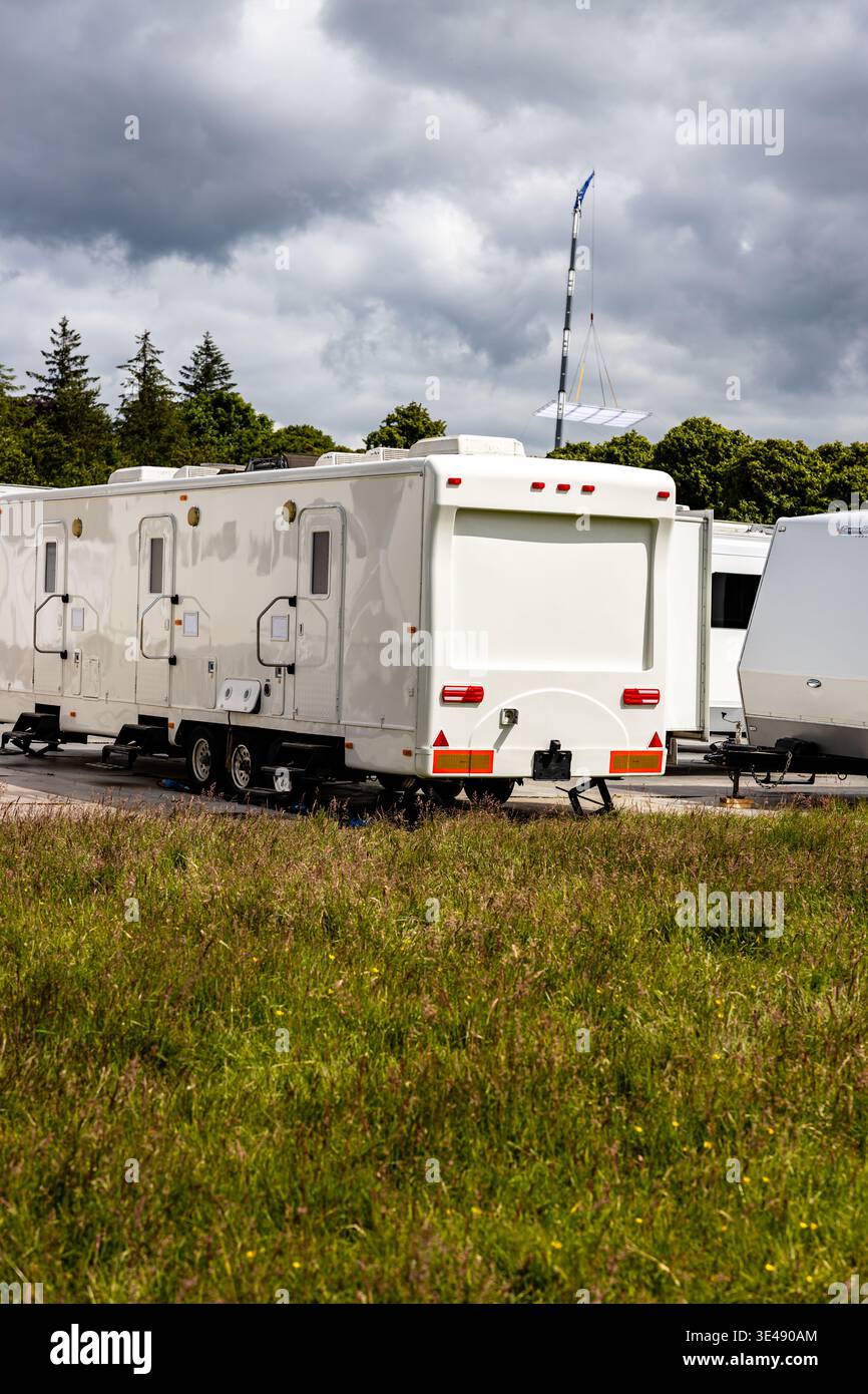 Servizi e servizi di localizzazione per TV e film, una fila di unità espandibili bianche o rimorchi da viaggio parcheggiati su un terreno solido e temporaneo con alberi Foto Stock