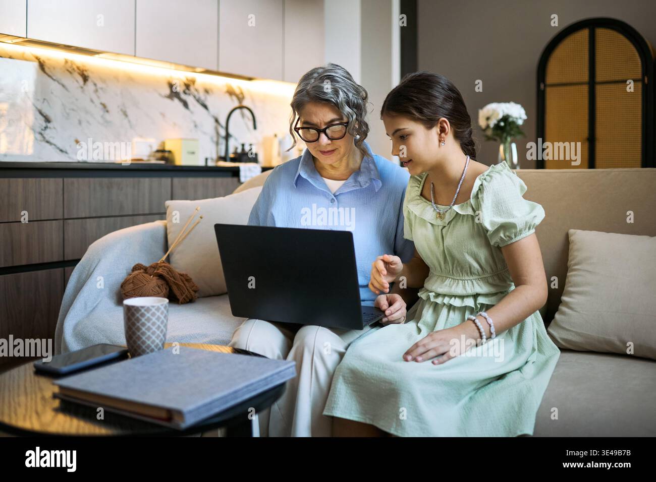 Donna anziana con nipote che utilizza un notebook mentre è seduta insieme, sfoglia contenuti online e condivide l'apprendimento digitale a casa. Utile per la tecnologia familiare, l'istruzione online, l'inclusione digitale Foto Stock