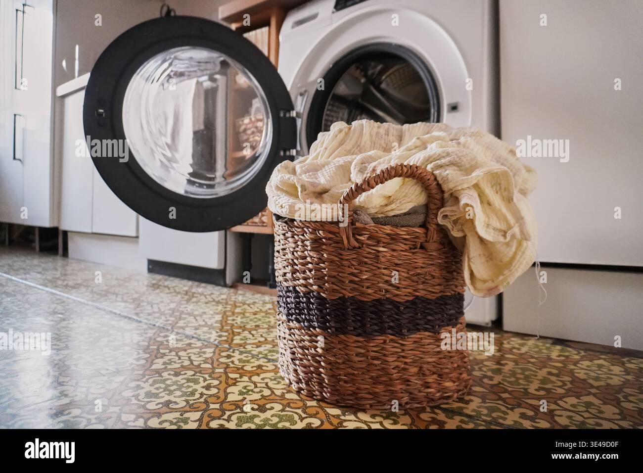 Cestino per lavanderia con pile di vestiti vicino alla lavatrice in un accogliente spazio interno Foto Stock