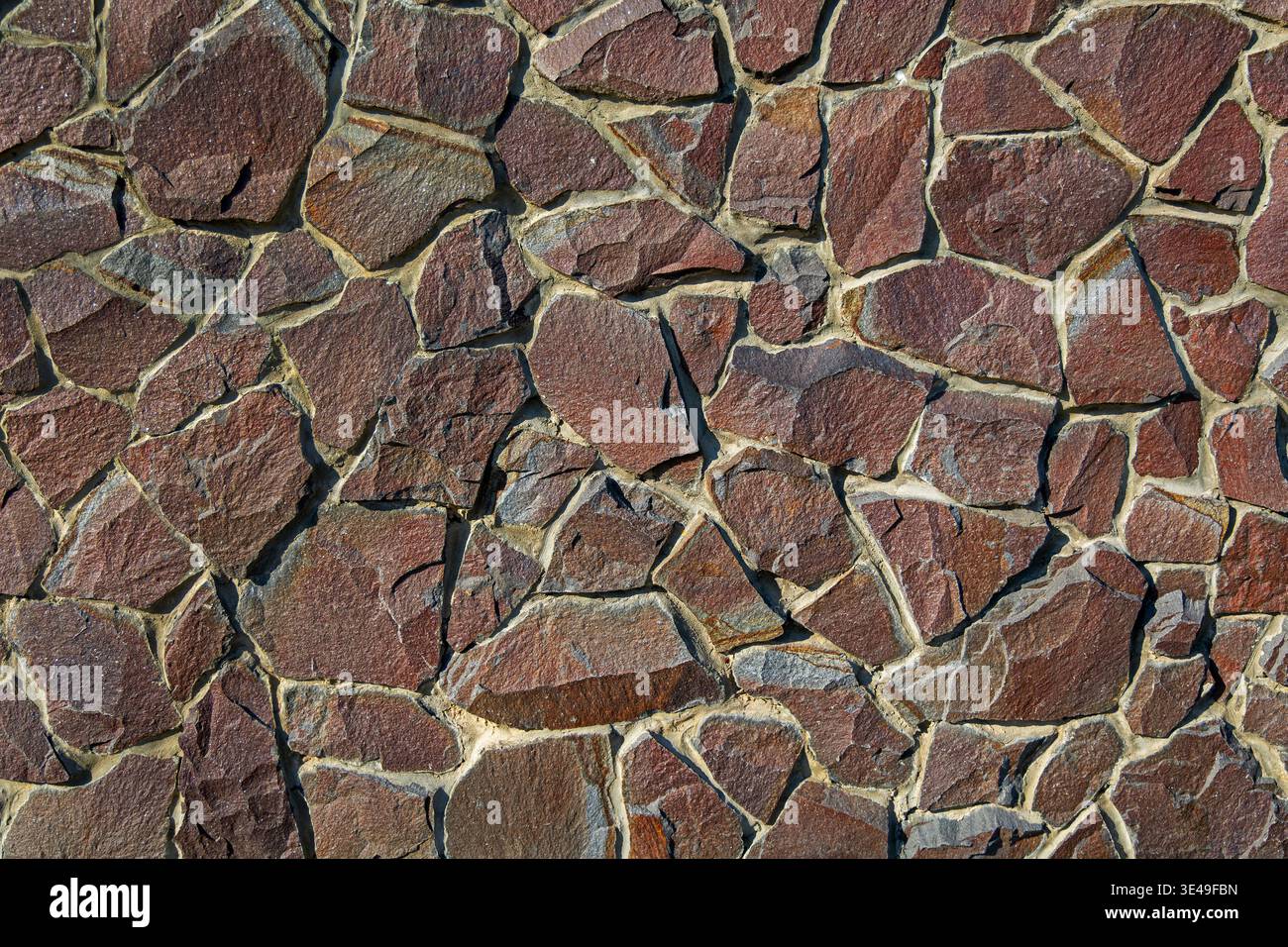 Sfondo irregolare della trama del muro di pietra marrone. Vista ravvicinata di un muro di pietra naturale irregolare con rocce marroni e rossastre, che creano una muratura robusta Foto Stock