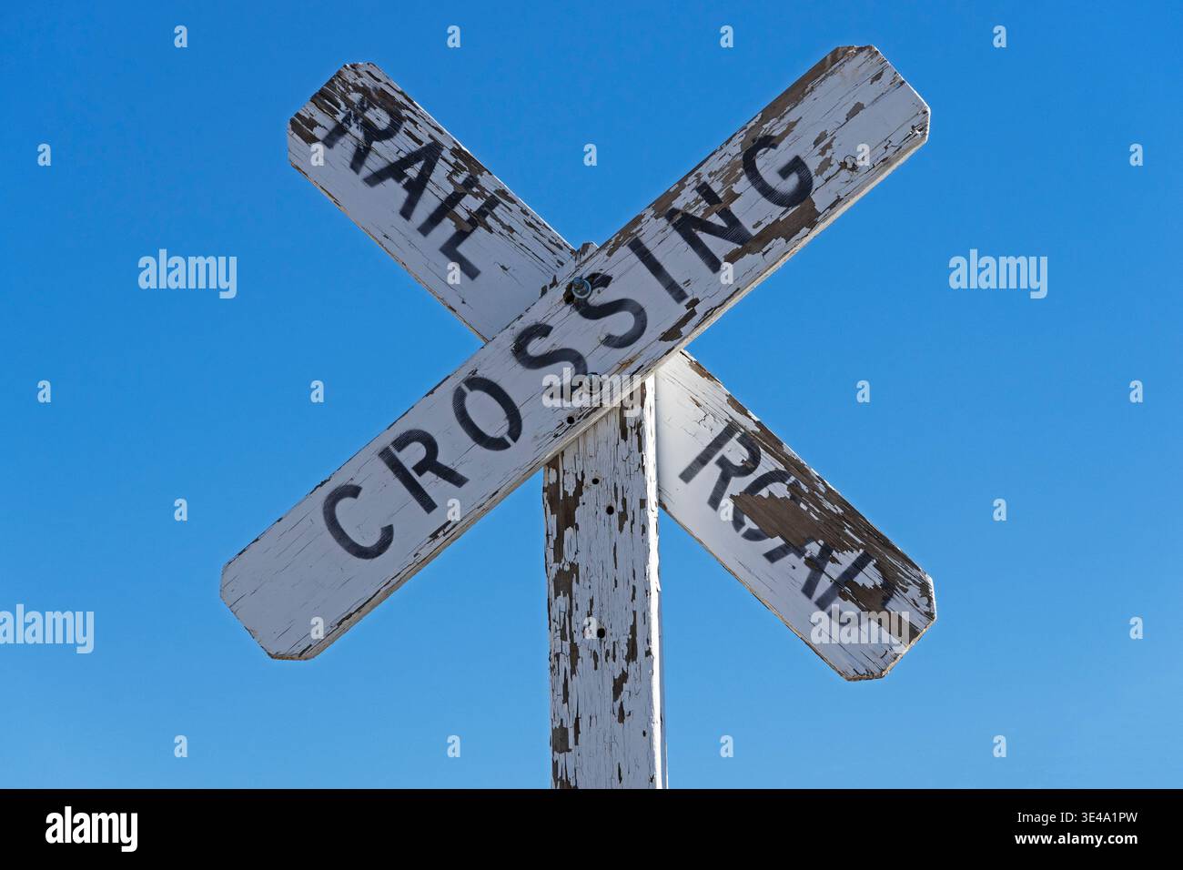 vecchio cartello di attraversamento della ferrovia in legno con vernice bianca sfalsata e sfondo blu del cielo Foto Stock