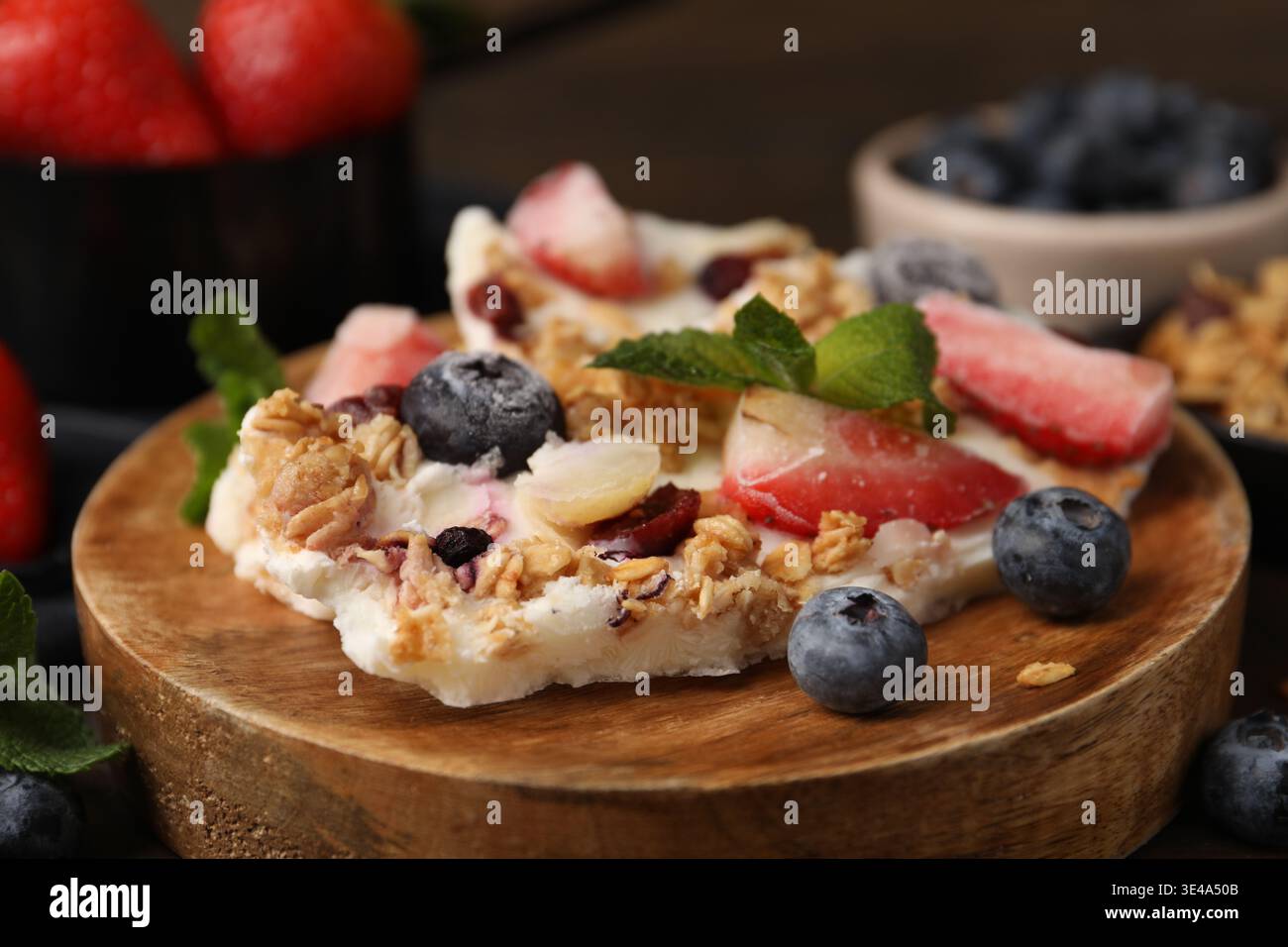 Pezzi di gustosa corteccia di yogurt con frutti di bosco, menta e muesli sul tavolo, primo piano Foto Stock