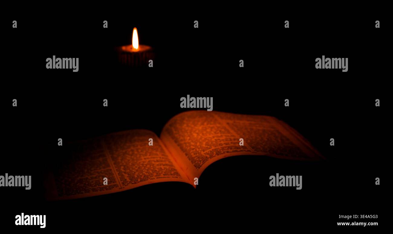 La luce delle candele risplende su un libro aperto in una stanza buia durante la notte Foto Stock