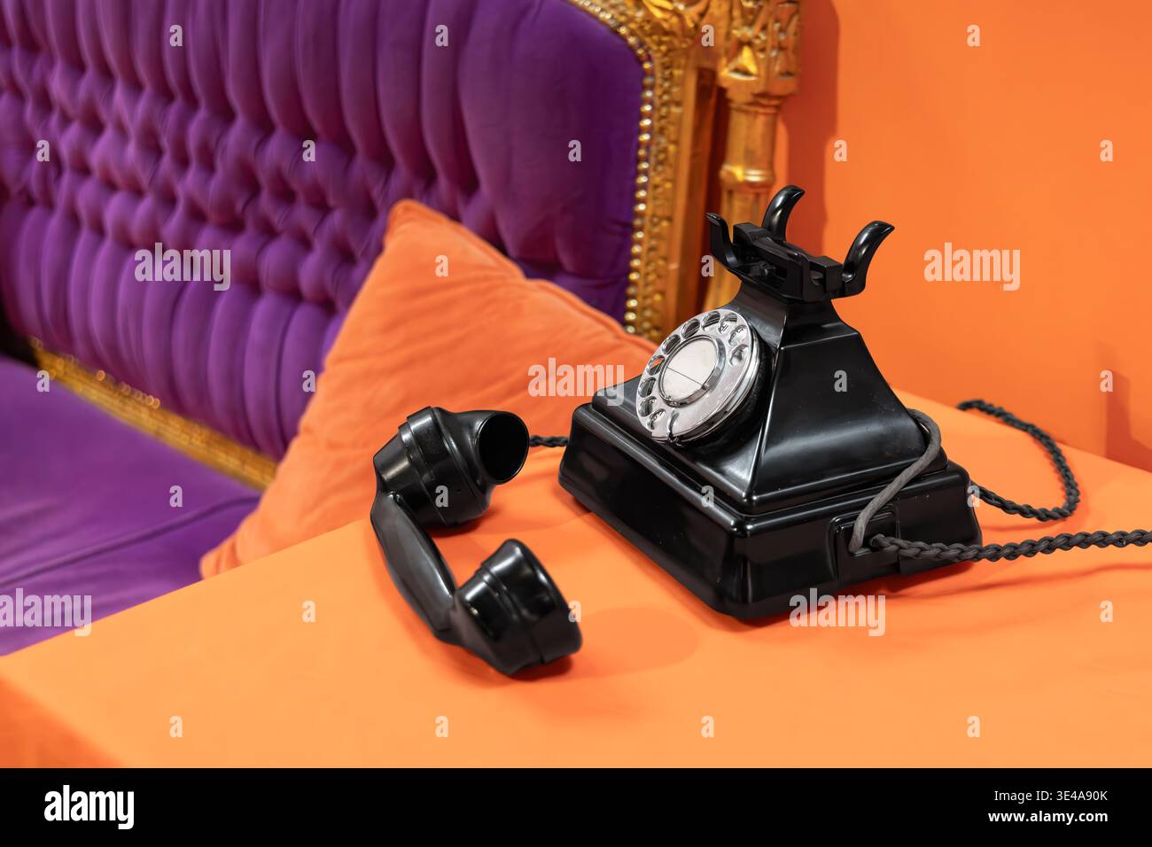 Telefono rotativo e ricevitore in bachelite vintage accanto alla sedia dorata e viola. Interni audaci in stile retrò che combinano comunicazione classica e arredi decorati Foto Stock