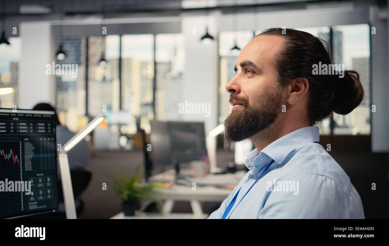 Commerciante in ufficio guardando verso l'alto con un sottile sorriso sul viso, visualizzando l'indipendenza finanziaria e il successo futuro. Broker di scorte ottimista alla scrivania dei PC che sogna ricchezza e libertà economica Foto Stock