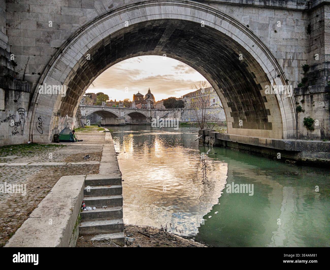 Le nuvole vicino al tramonto riflettono sull'acqua attraverso l'arco di un ponte sul fiume Tevere a Roma. Foto Stock