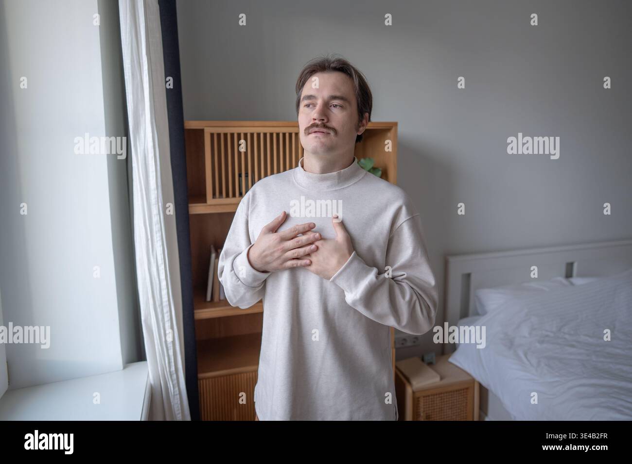Esercizio di consapevolezza con esercizi di respirazione profonda di uomo in piedi a finestra con le mani sul petto. Foto Stock