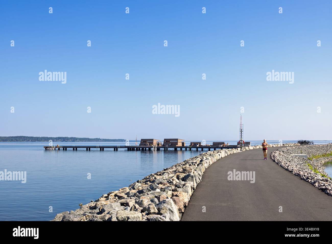 Donna che corre su una passerella vicino a un lago in una giornata estiva di sole Foto Stock
