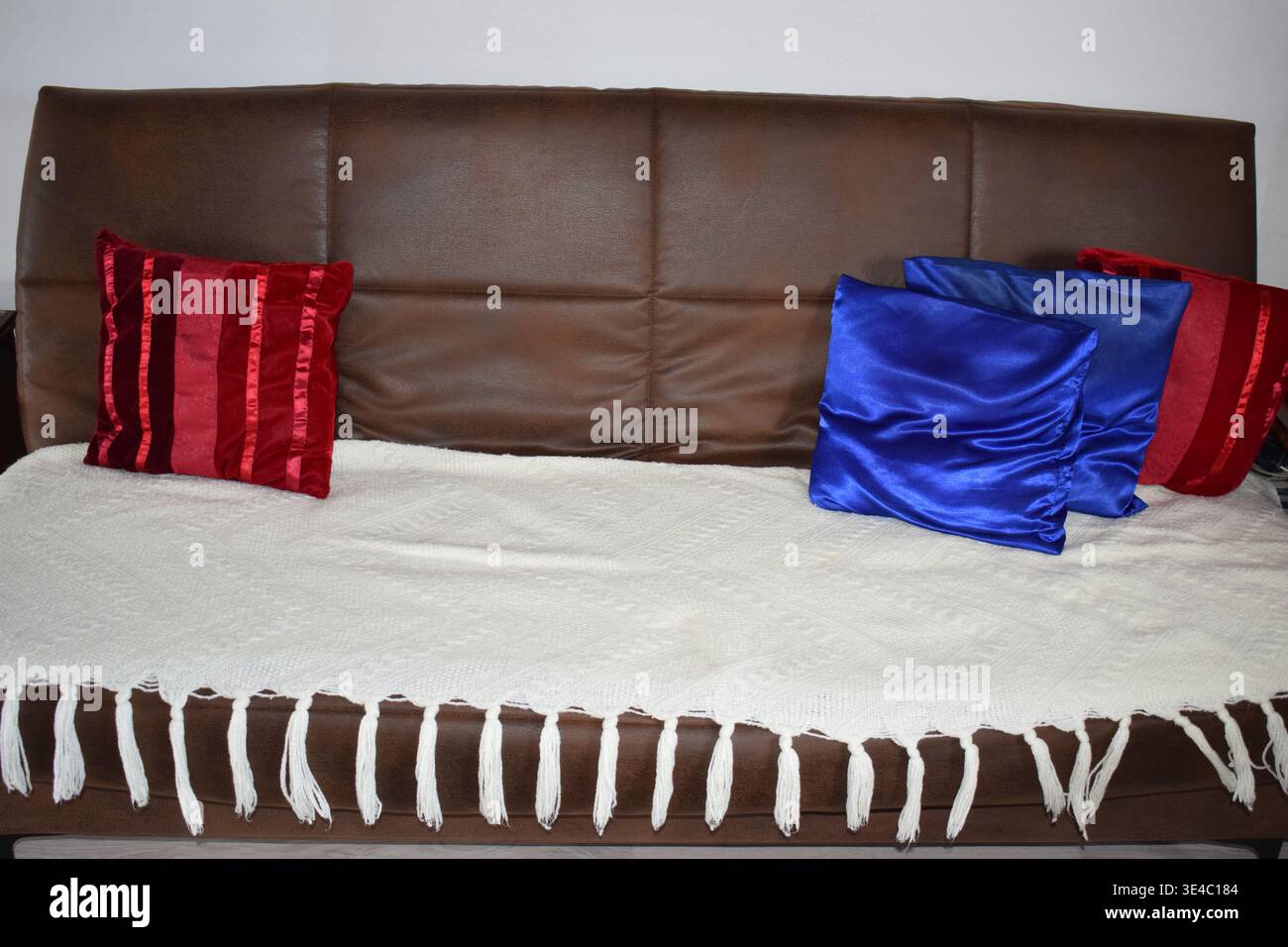 divano marrone con rivestimento bianco, decorazioni rosse e blu Foto Stock