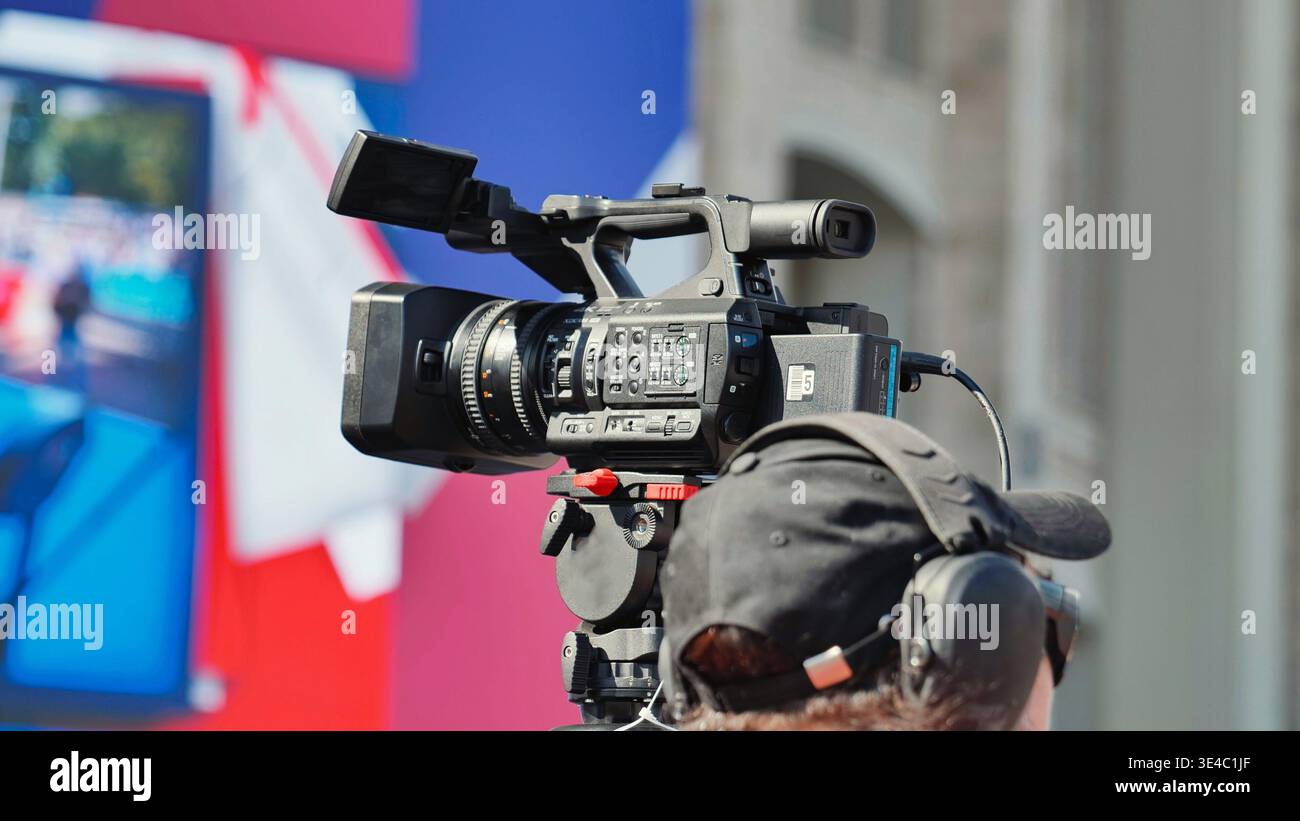 Cameraman con videocamera professionale che filma un evento dal vivo all'aperto. Foto Stock
