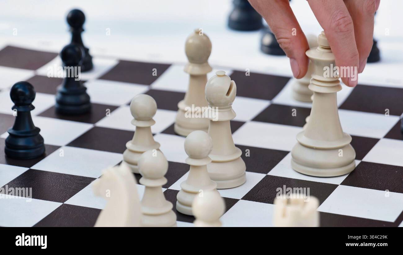 Primo piano di una mano che fa una mossa strategica con una scacchiera bianca su una tavola. Foto Stock