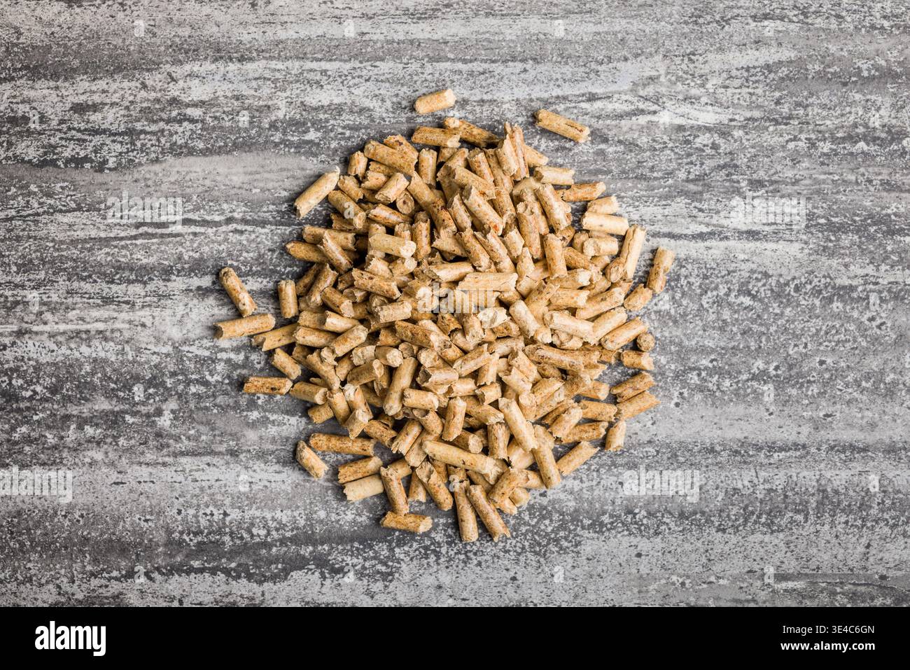 Piccoli pellet di legno dorato sparsi su una superficie di cemento testurizzato, che rappresentano combustibile da biomassa, riscaldamento rinnovabile, combustibile per stufe ed energia sostenibile Foto Stock