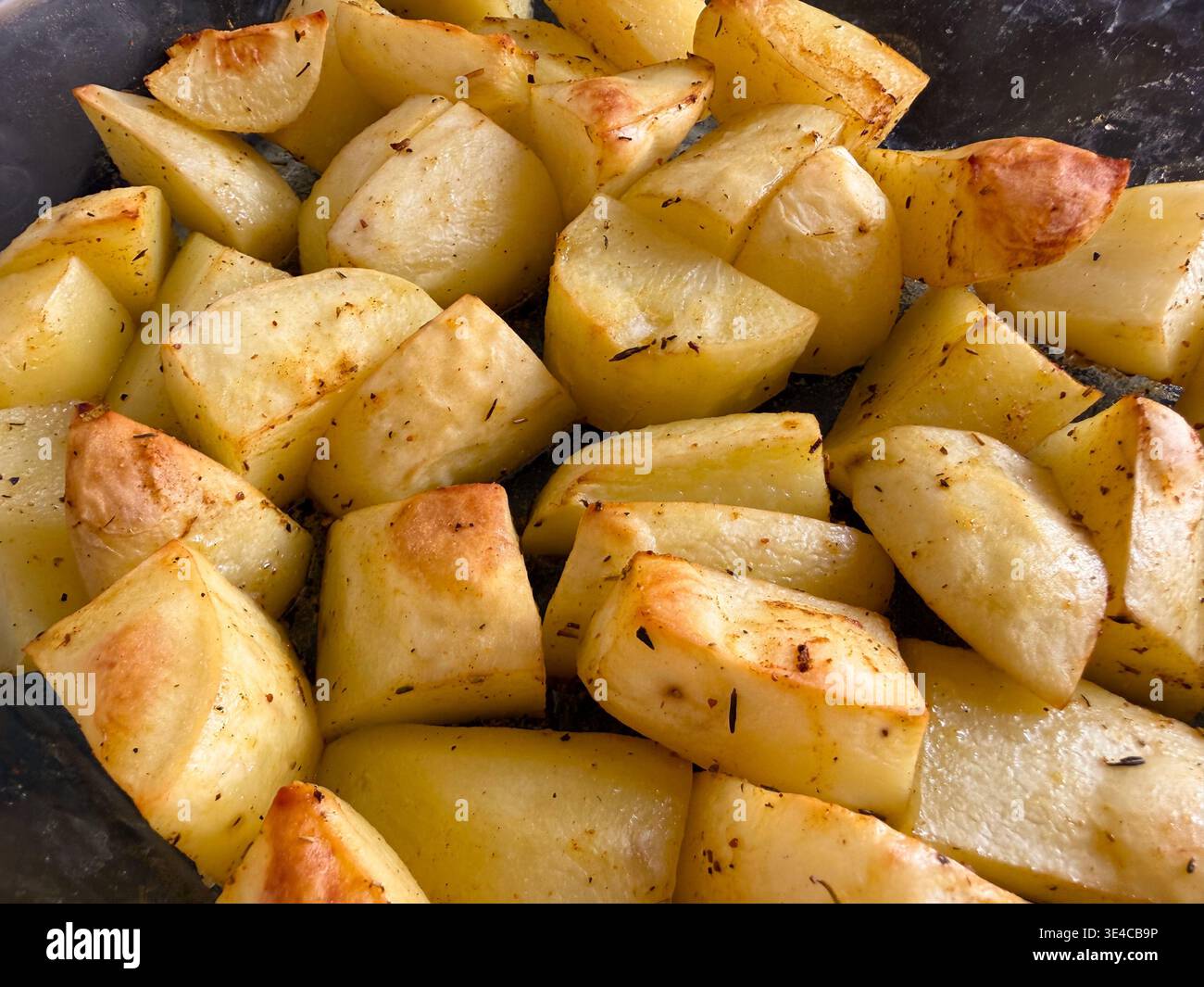 Primo piano di spicchi di patate arrosto dorate in una teglia da forno in vetro. - Immagine stock catturata con smartphone