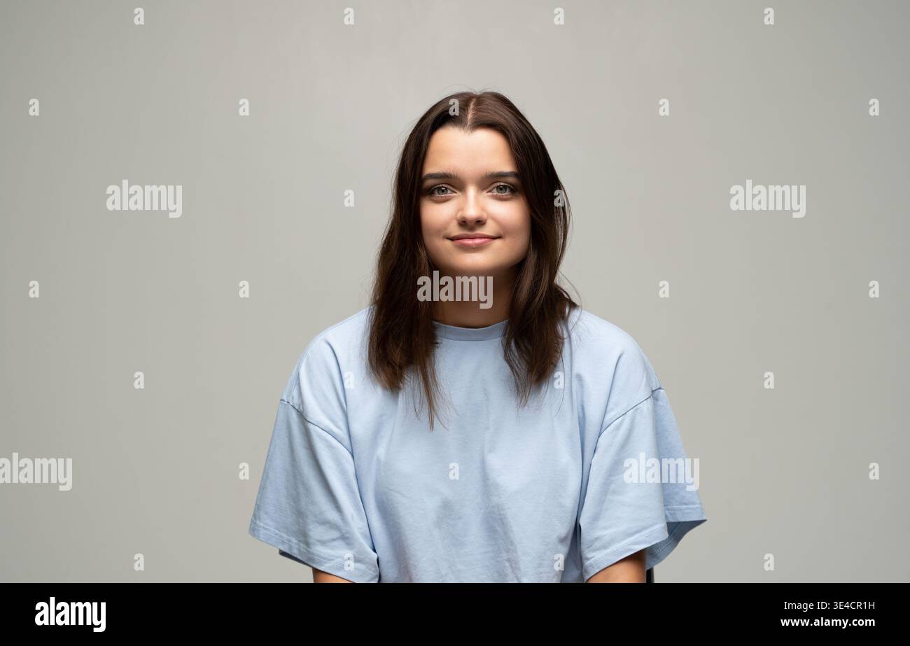 Giovane donna sorridente, che ha un contatto visivo nel ritratto di studio, che esprime positività e felicità in un ambiente informale Foto Stock