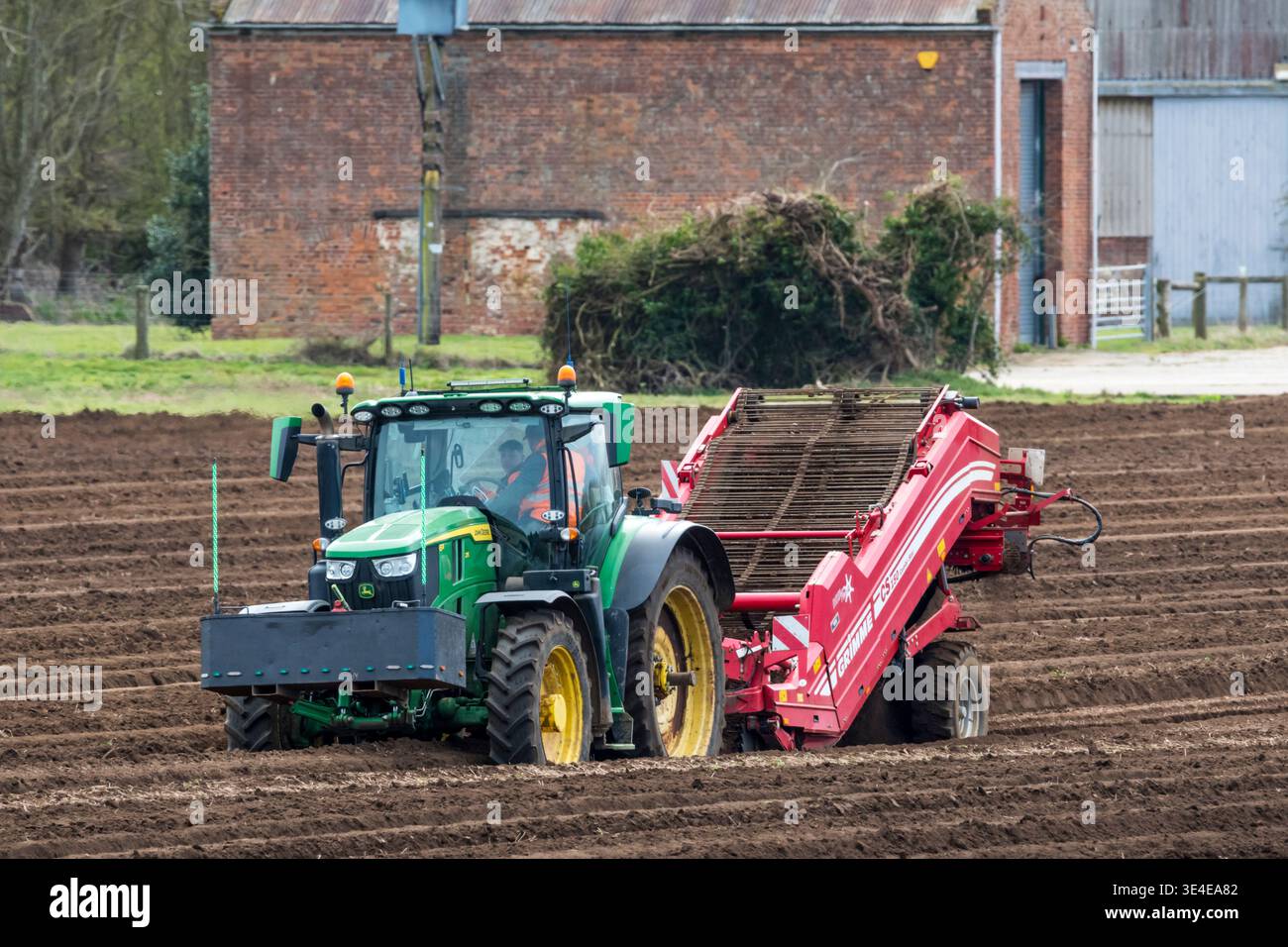Un trattore John Deere 6R che tira una Grimme destoner in un'azienda agricola a Norfolk. Preparazione del letto di semi per un raccolto di patate. Foto Stock