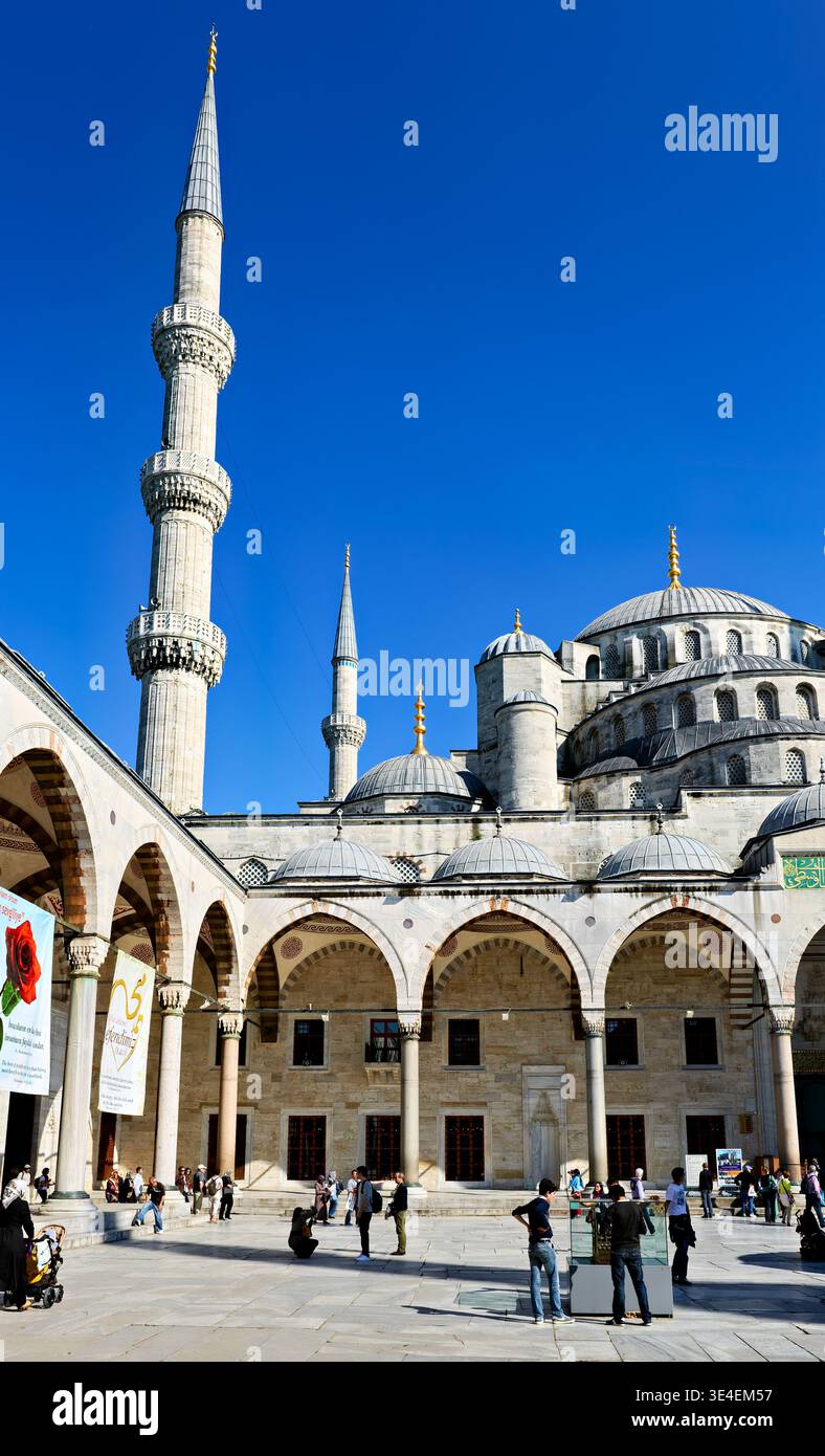 I visitatori esplorano la Moschea Blu di Istanbul sotto il cielo azzurro. Le persone ammirano l'architettura e scattano foto nel cortile. Foto Stock