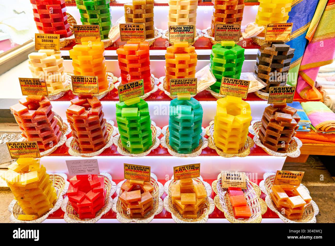 I venditori organizzano vari saponi colorati in pile per la vendita nel Grand Bazaar. Gli acquirenti cercano articoli unici nel mercato affollato. Foto Stock