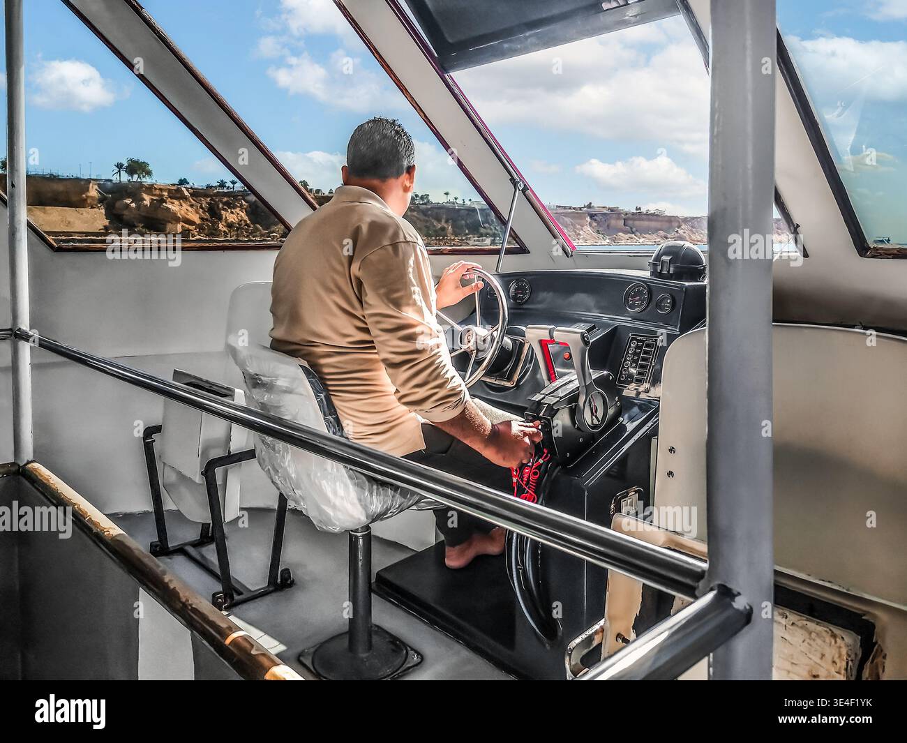 Il capitano di una nave turistica controlla la barca nella timoneria - vista dal retro. L'uomo si siede al volante. Sharm El Sheikh, Egitto - 19 gennaio 2020 Foto Stock