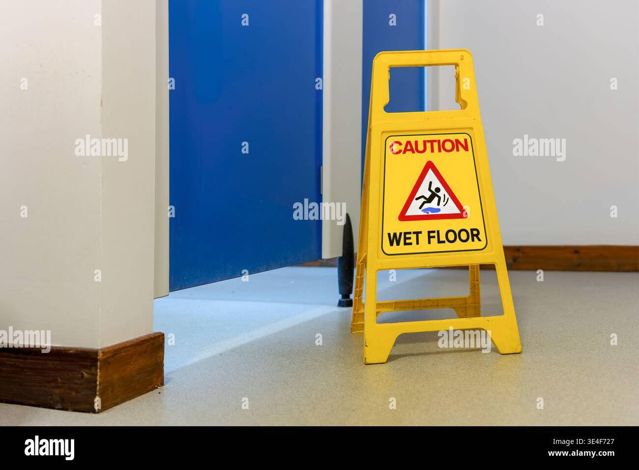 Foto ravvicinata a livello degli occhi del cartello di avvertimento giallo autoportante. Le parole "ATTENZIONE PAVIMENTO BAGNATO” e il grafico di slittamento internazionale sono chiaramente visibili. Foto Stock