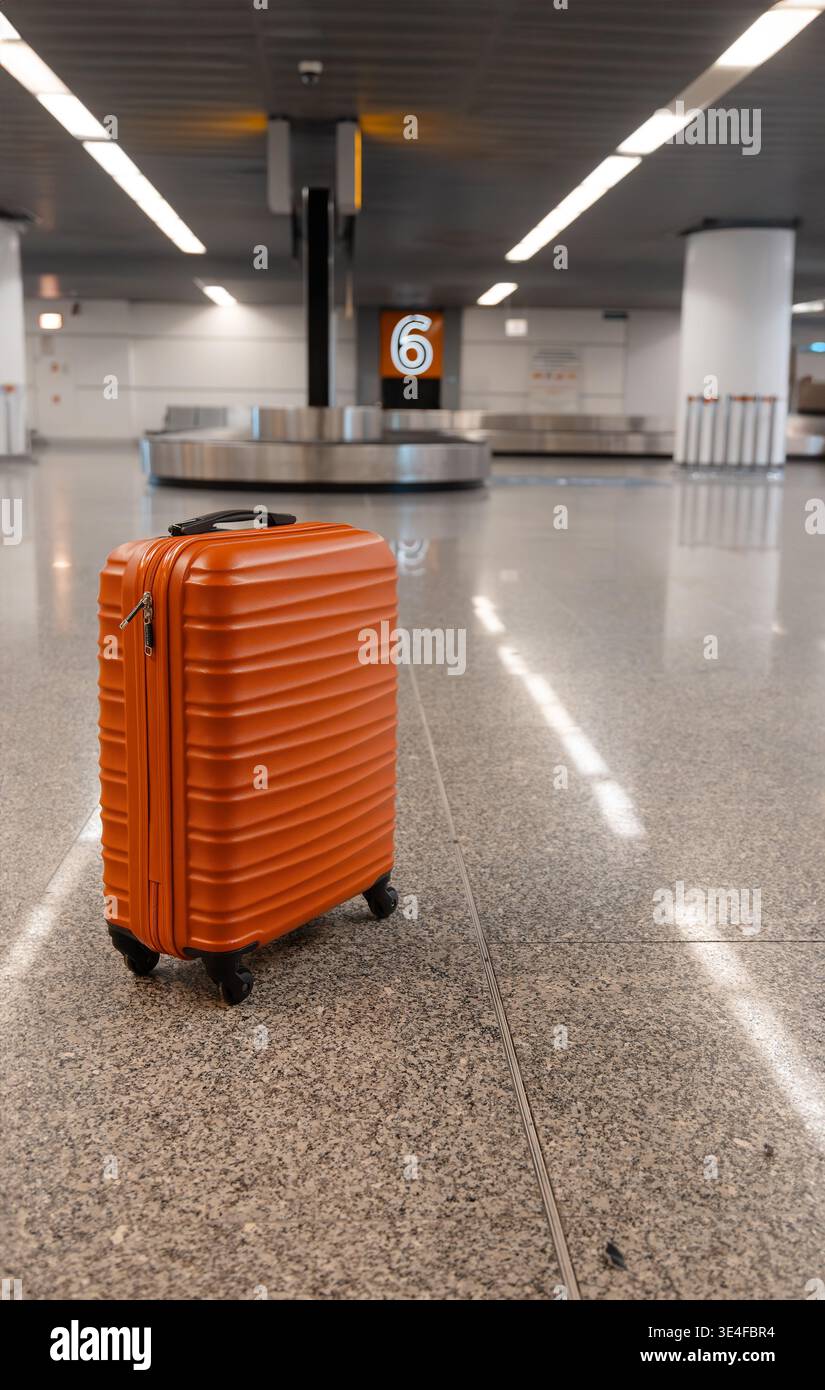 Valigia rossa in piedi nell'area di ritiro bagagli dell'aeroporto vicino alla giostra con il numero di targa nell'interno del terminal moderno. Foto Stock