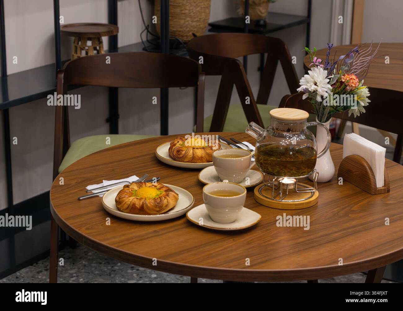 Due dolci a forma di fiore con pesca fresca e crema pasticcera, tazze da tè alle erbe e pentola di vetro su un tavolino da caffè in legno con vaso di fiori. Foto Stock