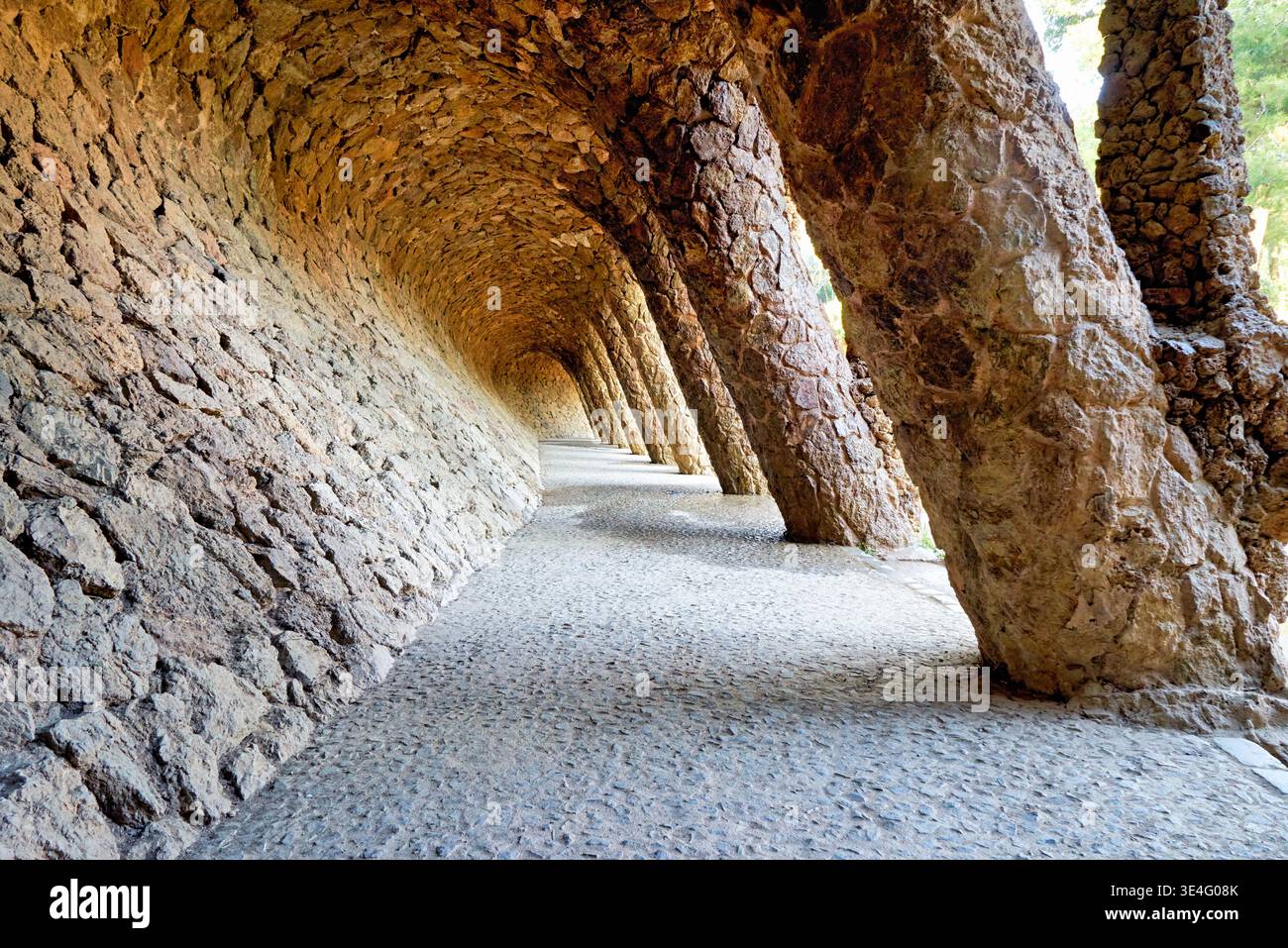 I visitatori camminano lungo un sentiero in pietra a Park Guell. Il percorso presenta archi e pietre uniche di Antoni Gaudi a Barcellona, Spagna. Foto Stock