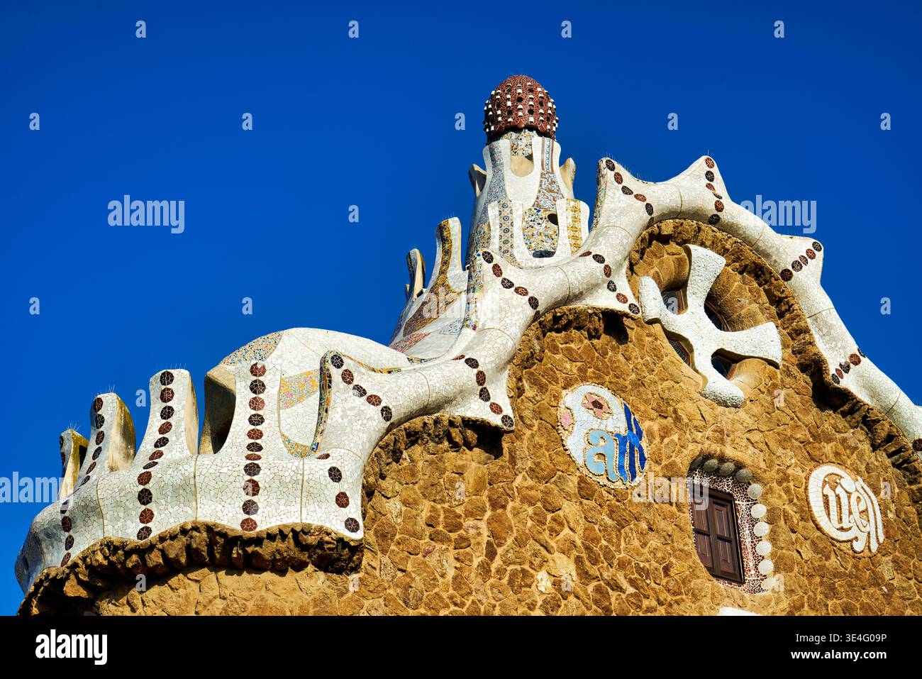 I visitatori osservano il tetto unico della Casa delle fiabe a Park Guell, un punto di riferimento a Barcellona, in Spagna, sotto un cielo azzurro. Foto Stock