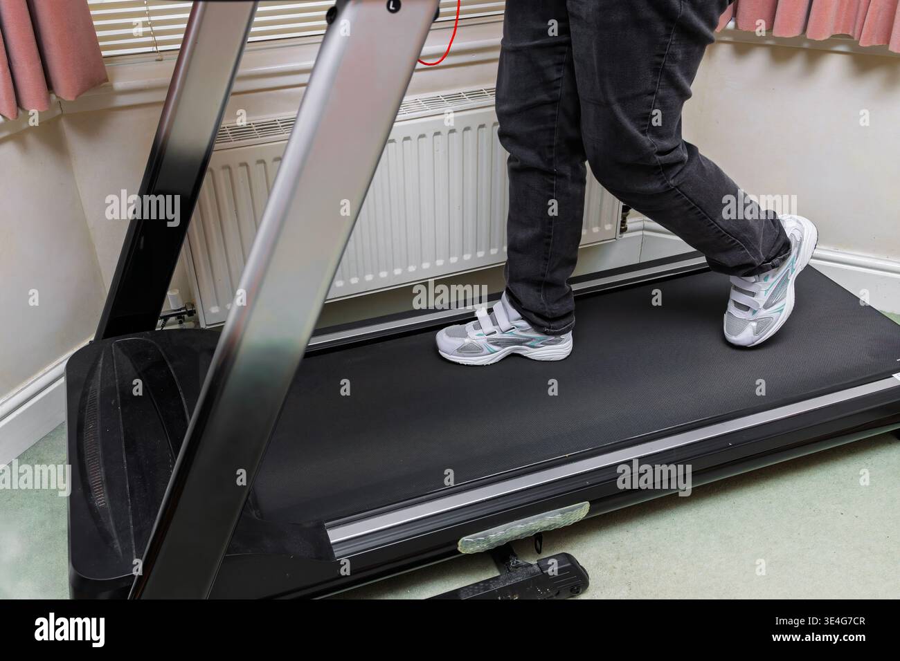 L'angolo laterale del tapis roulant che cammina nel soggiorno domestico mostra un comodo allenamento al coperto e la routine quotidiana di fitness Foto Stock