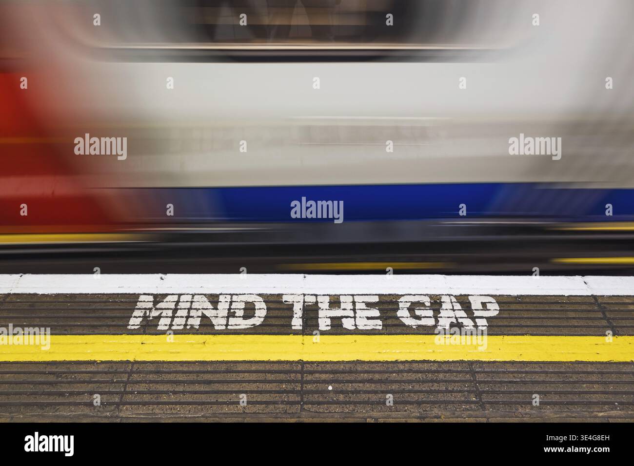 TENERE PRESENTE IL messaggio di sicurezza GAP su una piattaforma della metropolitana di Londra, mentre un treno della metropolitana in velocità si sfuma nel passato, illustrando la prudenza del transito urbano e la trave ferroviaria del Regno Unito Foto Stock