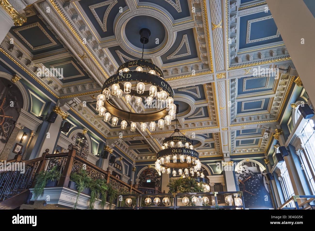 Lobby di epoca vittoriana con soffitto a cassettoni color tè, lampadari luminosi, scalinata in legno e vegetazione, catturati da un'angolazione bassa per mettere in risalto l'ornato pla Foto Stock