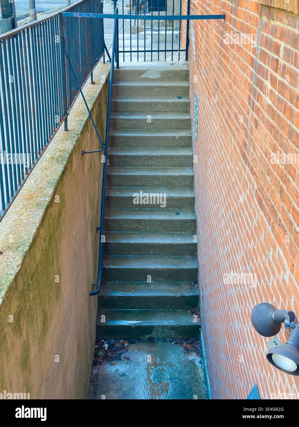 Le scale in cemento scendono da un muro di mattoni marroni fino a un sentiero sottostante. Una ringhiera corre lungo le scale. La scena è ambientata in un'area urbana con un cle Foto Stock