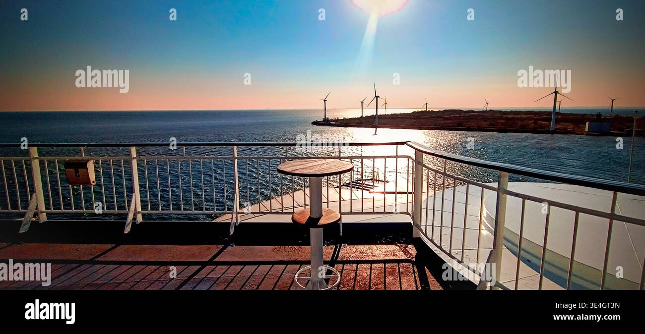 Vista dal ponte dei traghetti con tavolo e ringhiera verso il mare e le turbine eoliche offshore al tramonto, viaggi marittimi e scenari di energia rinnovabile. Foto Stock