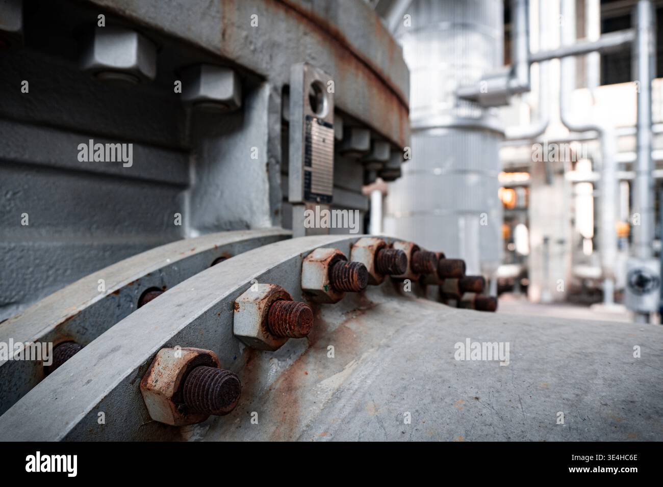 Primo piano di bulloni arrugginiti sul tubo industriale. Macchinari pesanti in background. Impostazione industriale con superfici metalliche usurate. Adatto per ingegneria, manu Foto Stock