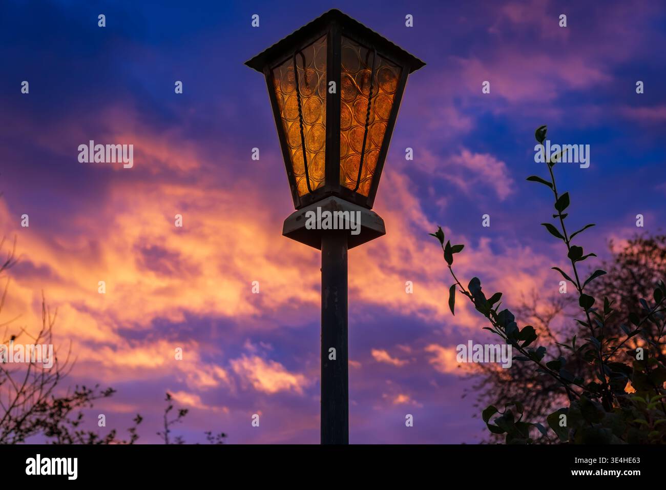 Vista ravvicinata di un lampione stradale d'epoca che si illumina al crepuscolo contro un cielo colorato al tramonto con nuvole spettacolari. Atmosfera notturna. Foto Stock