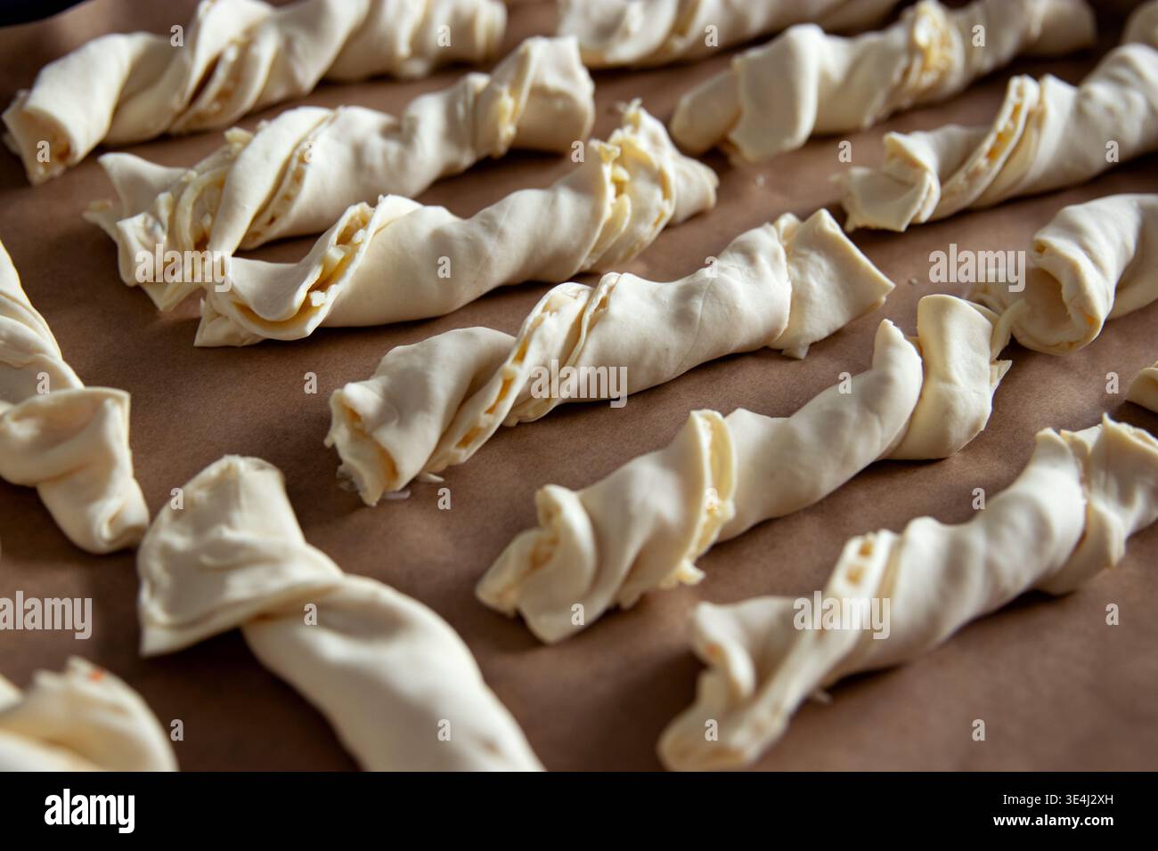 Impasto di pasta cruda ritorta sistemato ordinatamente su una teglia da forno rivestita di carta pergamena, pronto per la cottura in cucina con illuminazione naturale Foto Stock
