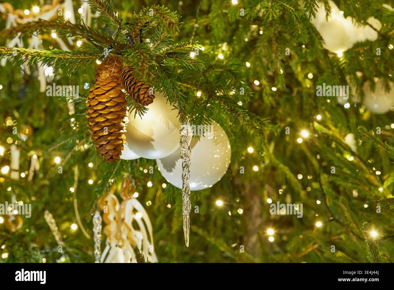 Primo piano di alberi di Natale decorati con coni di pino, ornamenti bianchi e calde luci festive Foto Stock