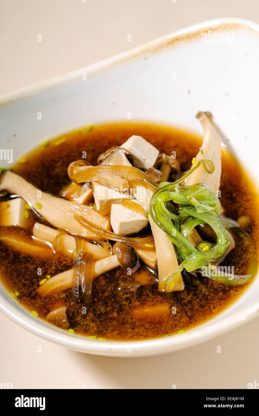 Primo piano della zuppa giapponese di miso in una ciotola, realizzata con pasta di miso e brodo dashi, cubetti di tofu, funghi shiitake ed enoki, alghe wakame e verde su Foto Stock